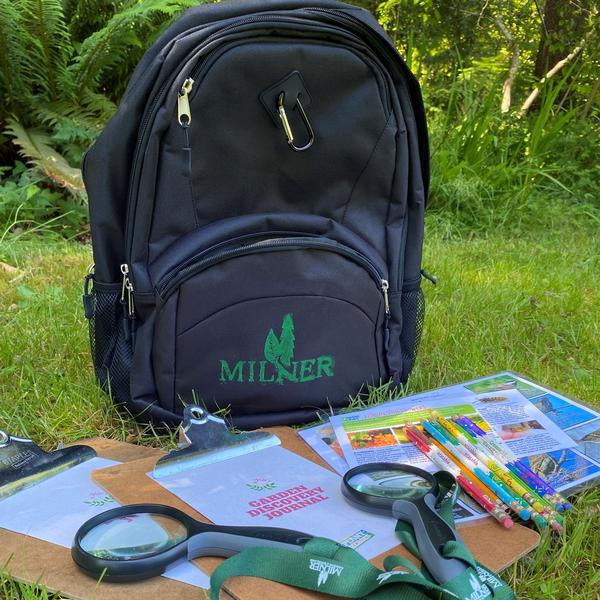 A black backpack on the grass with clipboards, identification sheets, and magnifying glasses