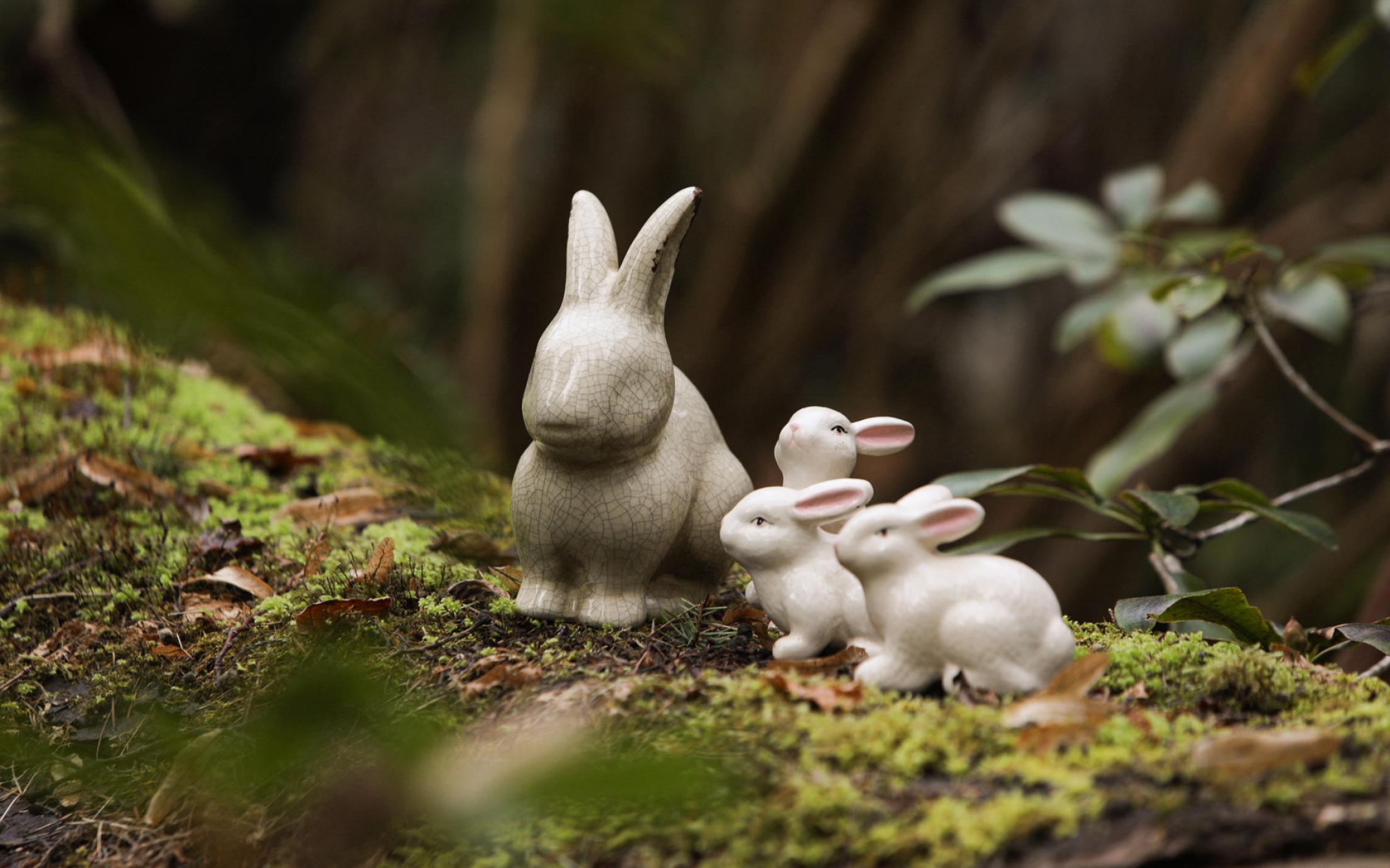 Decorative ceramic bunnies sitting on a mossy stump in the forest.