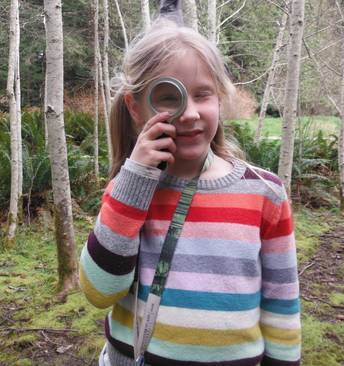 Blond child in striped sweater looking at the camera through a magnifying class
